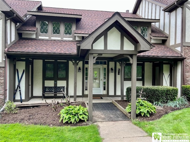 view of exterior entry featuring covered porch, a shingled roof, and stucco siding