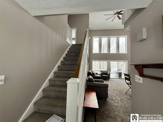 stairway with carpet, a high ceiling, a ceiling fan, a textured ceiling, and baseboards