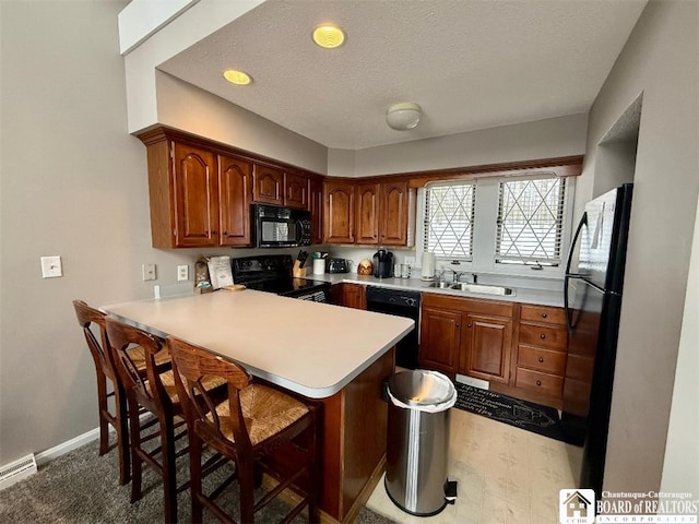 kitchen with light countertops, a sink, a peninsula, and black appliances