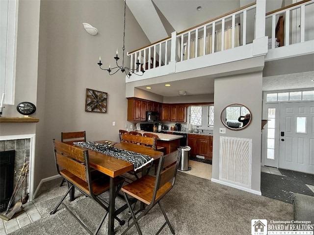 dining room featuring light carpet, visible vents, a tile fireplace, an inviting chandelier, and a high ceiling