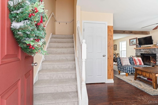 stairway with ceiling fan, a stone fireplace, and wood finished floors