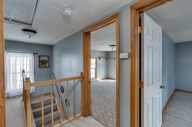 hallway with light carpet, a textured ceiling, an upstairs landing, and baseboards