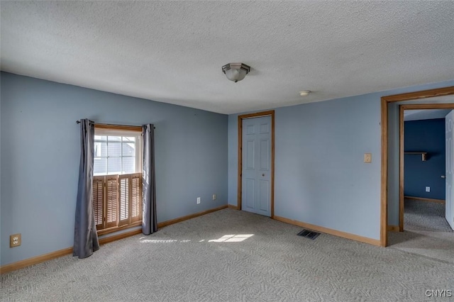 spare room with baseboards, a textured ceiling, visible vents, and light colored carpet