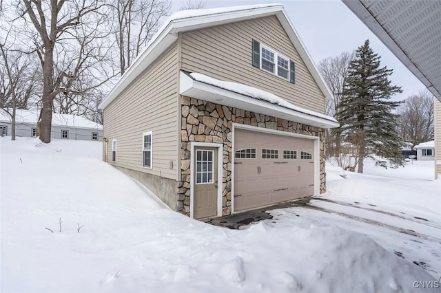 snow covered property with a garage and stone siding