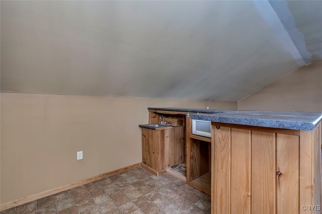 additional living space with baseboards, stone finish floor, wet bar, and vaulted ceiling