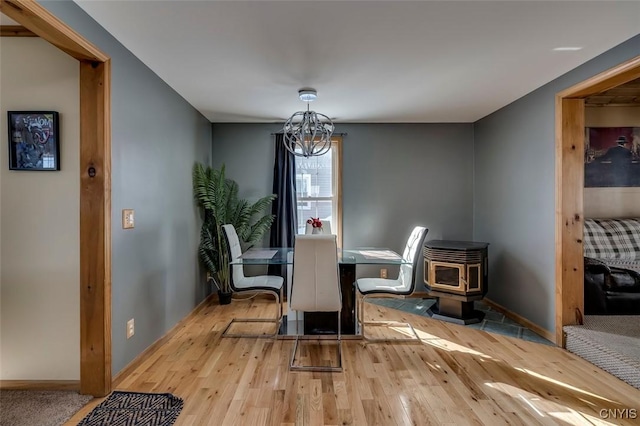 dining area with baseboards, light wood finished floors, a wood stove, and an inviting chandelier