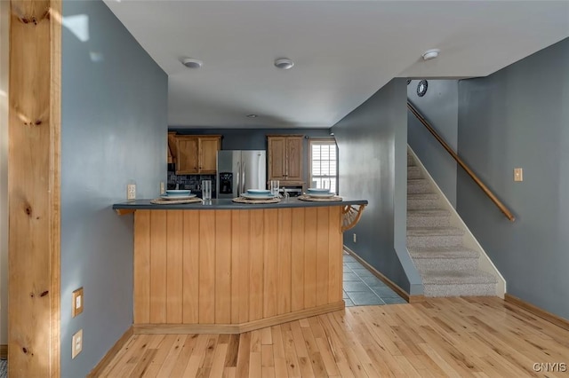 kitchen with dark countertops, brown cabinets, a peninsula, and stainless steel fridge with ice dispenser