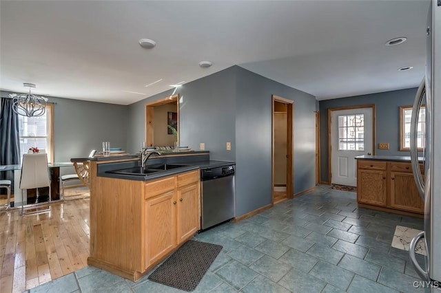 kitchen with baseboards, dark countertops, hanging light fixtures, stainless steel appliances, and a sink