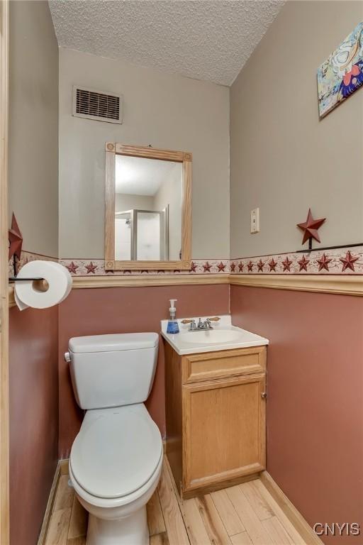 bathroom featuring visible vents, toilet, wood finished floors, a textured ceiling, and vanity