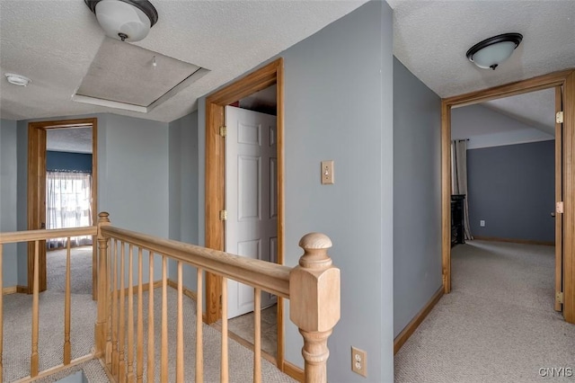 corridor featuring light carpet, a textured ceiling, an upstairs landing, and baseboards