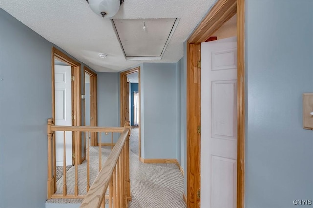 hallway with attic access, carpet flooring, an upstairs landing, and baseboards