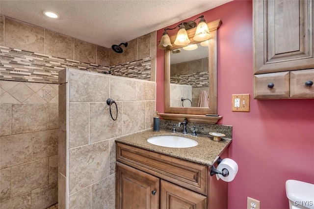 full bath featuring toilet, tiled shower, a textured ceiling, and vanity