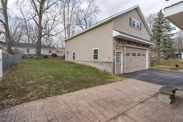 view of property exterior featuring aphalt driveway, a lawn, stone siding, fence, and an attached garage