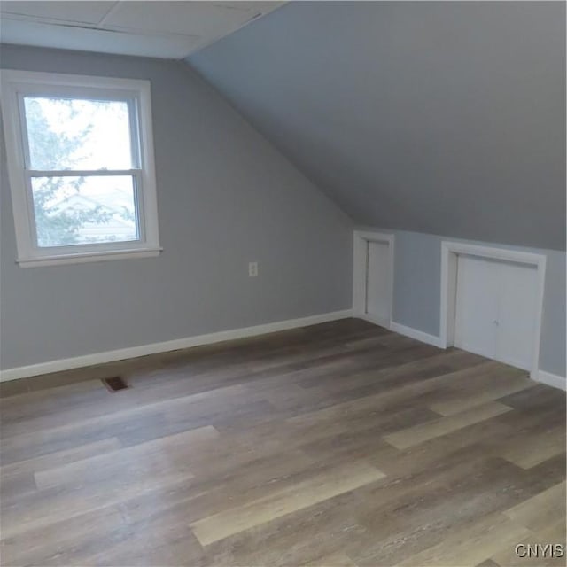 additional living space with lofted ceiling, wood finished floors, visible vents, and baseboards