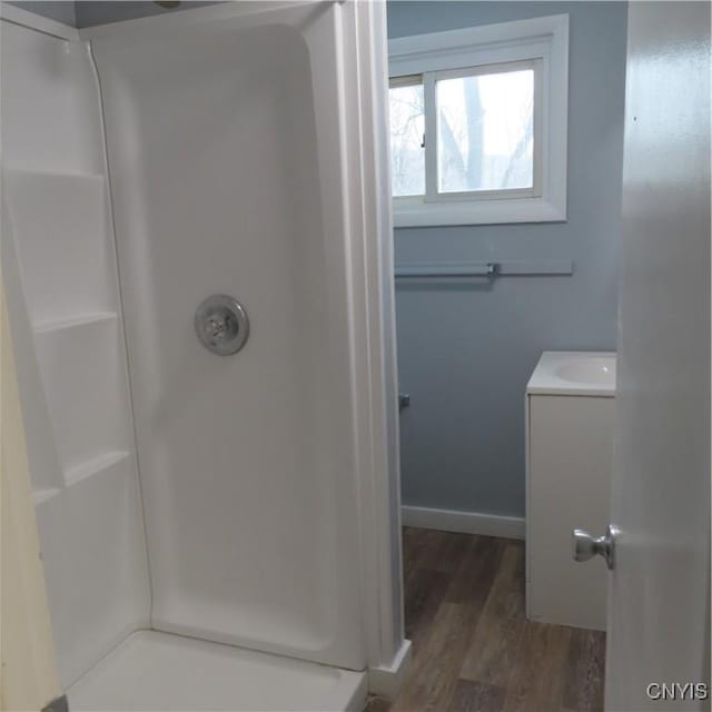 bathroom with a shower, wood finished floors, vanity, and baseboards