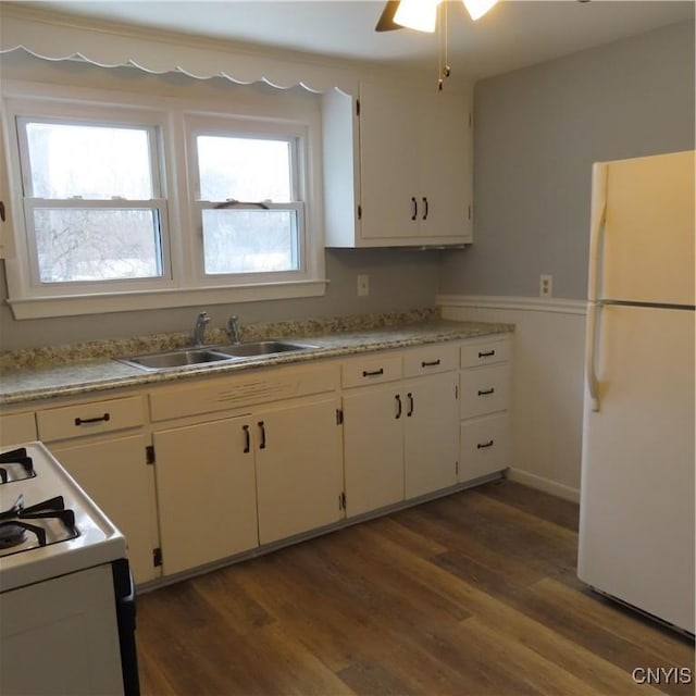 kitchen with light countertops, dark wood-type flooring, white cabinets, a sink, and white appliances