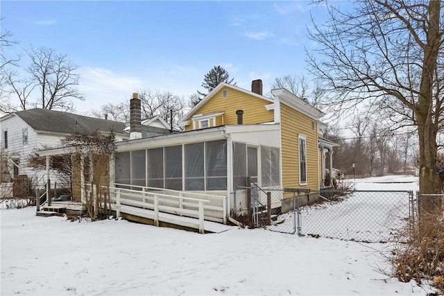 snow covered rear of property with a chimney, fence, and a sunroom