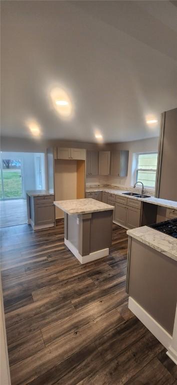 kitchen with a kitchen island, light stone counters, dark wood finished floors, and a sink