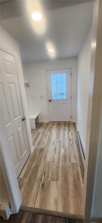 doorway featuring a baseboard heating unit, light wood-style flooring, and baseboards