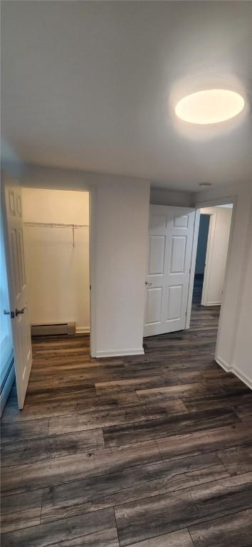 interior space with baseboards, a baseboard heating unit, and dark wood-type flooring