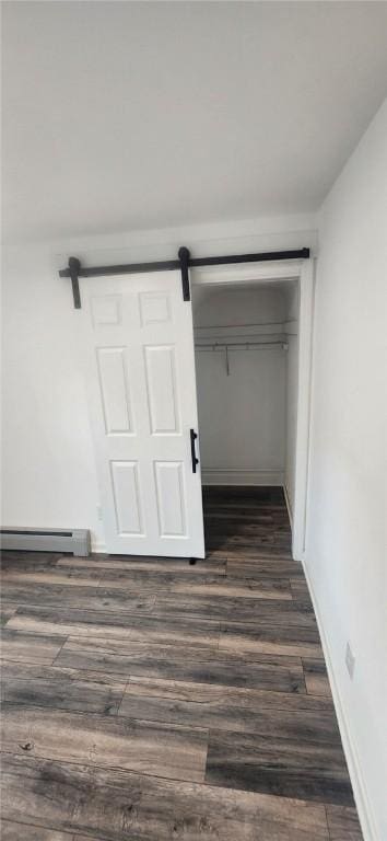 unfurnished bedroom featuring a barn door, baseboard heating, dark wood finished floors, and baseboards