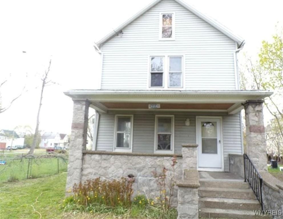 american foursquare style home with covered porch, stone siding, and fence