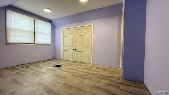 unfurnished bedroom featuring lofted ceiling, a closet, wood finished floors, and visible vents