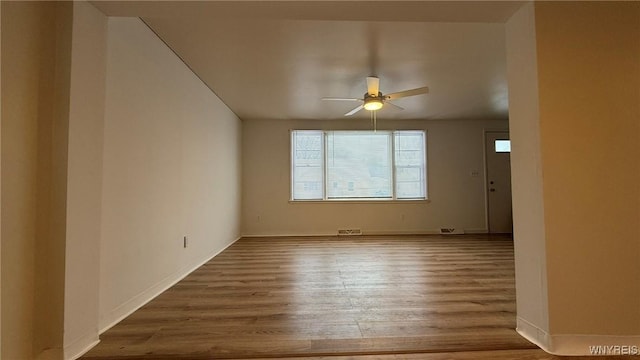 unfurnished room with a ceiling fan, visible vents, baseboards, and wood finished floors