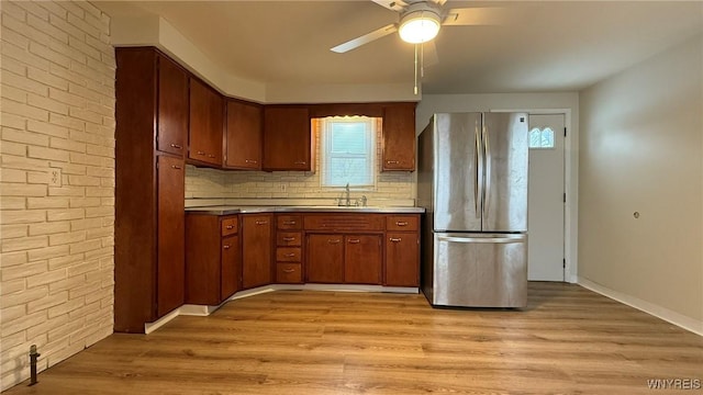 kitchen with light wood-style flooring, decorative backsplash, freestanding refrigerator, a sink, and ceiling fan