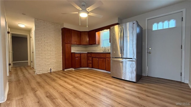 kitchen with decorative backsplash, freestanding refrigerator, a sink, and light wood finished floors