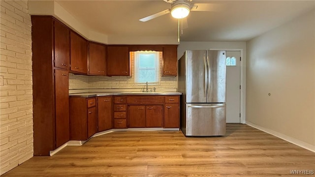 kitchen featuring a sink, light wood-type flooring, freestanding refrigerator, brown cabinets, and tasteful backsplash