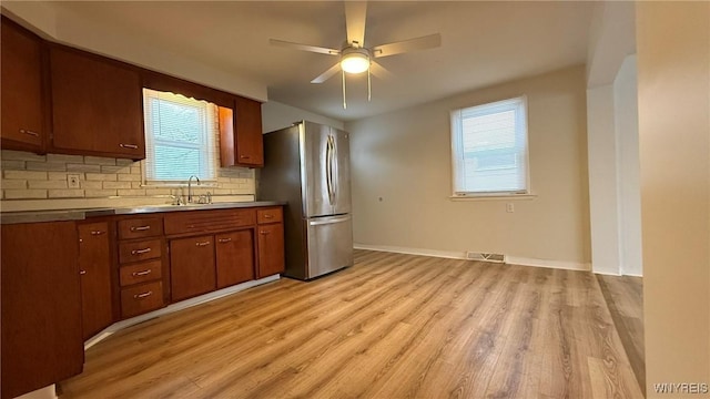 kitchen featuring a sink, a ceiling fan, freestanding refrigerator, light wood finished floors, and tasteful backsplash