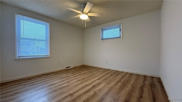 empty room with ceiling fan, wood finished floors, visible vents, and baseboards