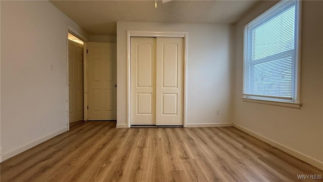 unfurnished bedroom featuring a textured ceiling, light wood-style floors, a closet, and baseboards