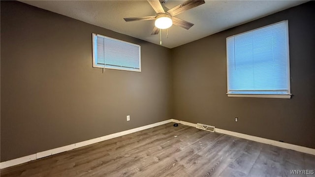 spare room featuring a ceiling fan, wood finished floors, visible vents, and baseboards