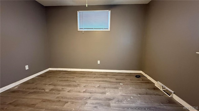 spare room featuring baseboards, visible vents, and wood finished floors