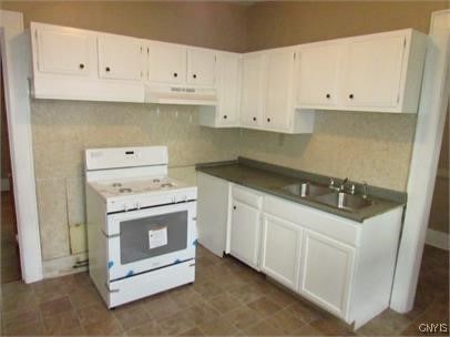 kitchen featuring dark countertops, white cabinets, a sink, under cabinet range hood, and white gas range oven