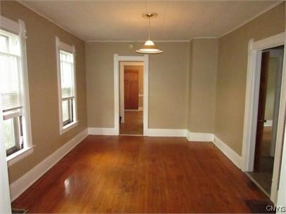 unfurnished dining area featuring baseboards, ornamental molding, and wood finished floors