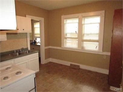 kitchen featuring dark countertops, visible vents, white cabinetry, a sink, and baseboards