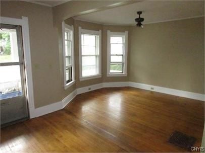 empty room with crown molding, baseboards, arched walkways, and wood finished floors