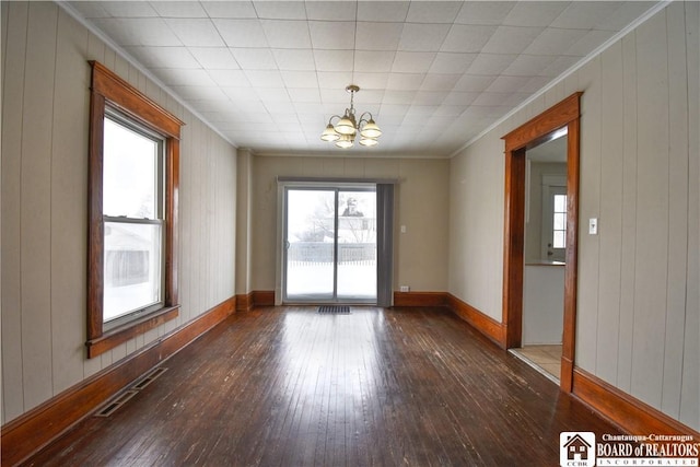 spare room with baseboards, visible vents, dark wood-style floors, ornamental molding, and an inviting chandelier