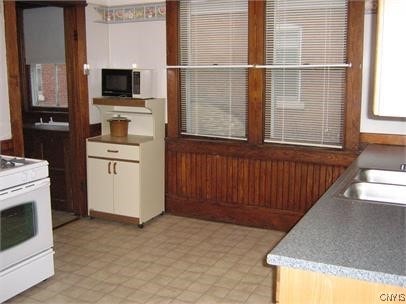 kitchen featuring white gas stove, light countertops, white cabinets, a sink, and black microwave