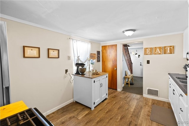 kitchen with light wood finished floors, visible vents, dark countertops, ornamental molding, and white cabinetry