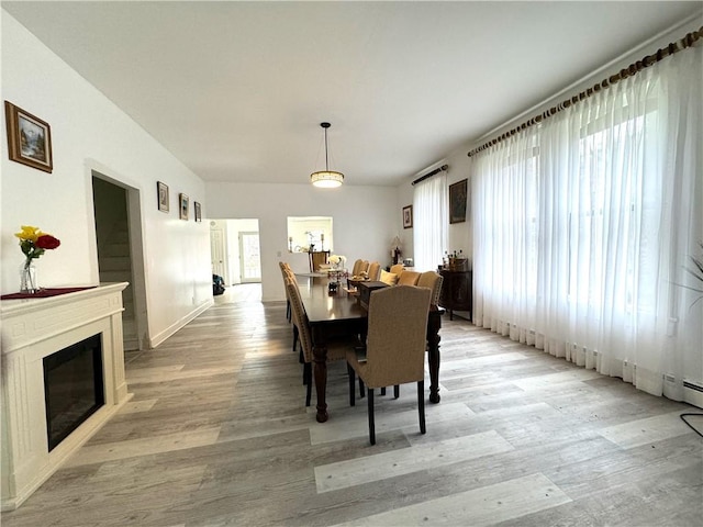 dining area with light wood-type flooring and a glass covered fireplace