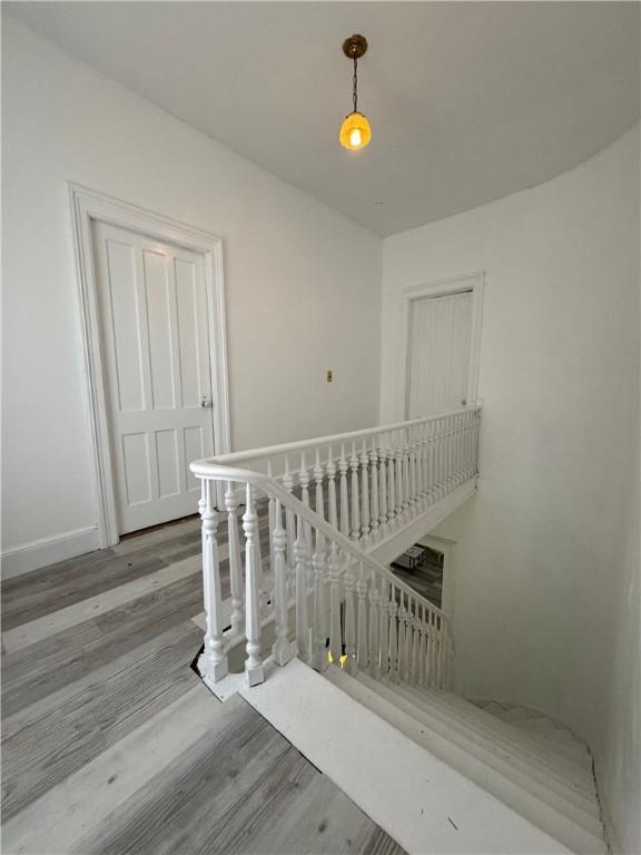 corridor featuring wood finished floors, an upstairs landing, and baseboards