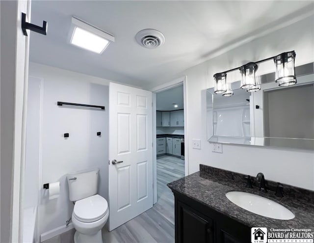 bathroom with toilet, visible vents, wood finished floors, and vanity