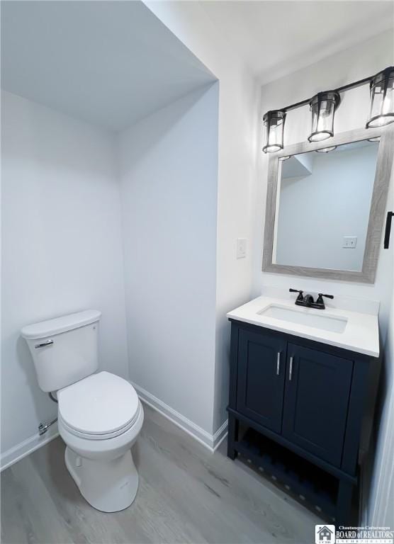 half bathroom with toilet, baseboards, wood finished floors, and vanity