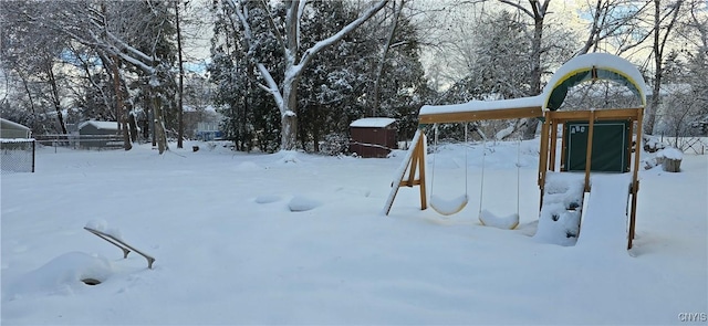 yard layered in snow featuring a garage, fence, and a playground