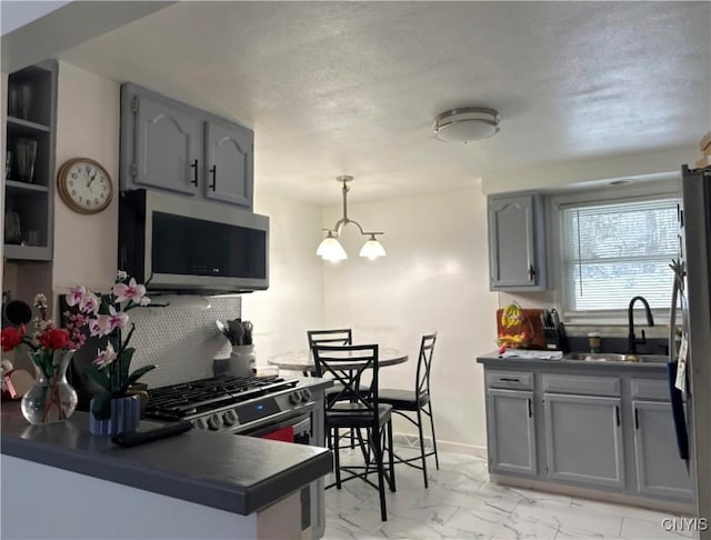 kitchen with stainless steel appliances, a sink, marble finish floor, hanging light fixtures, and dark countertops