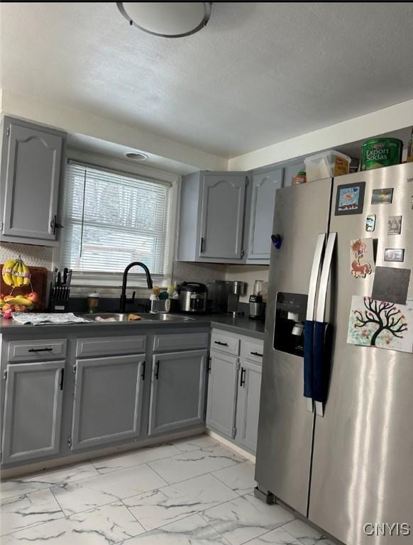 kitchen with stainless steel fridge, dark countertops, marble finish floor, gray cabinetry, and a sink